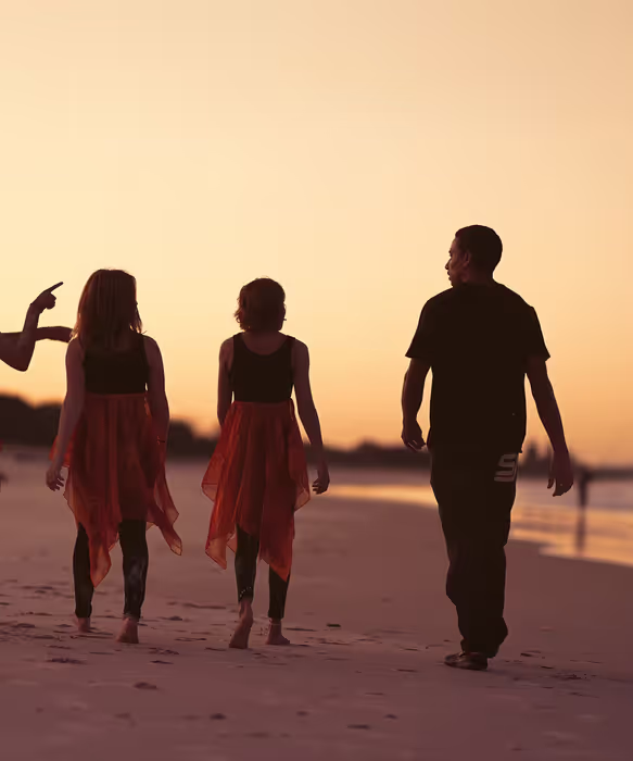 4 young adults walking down a beach at sunset.